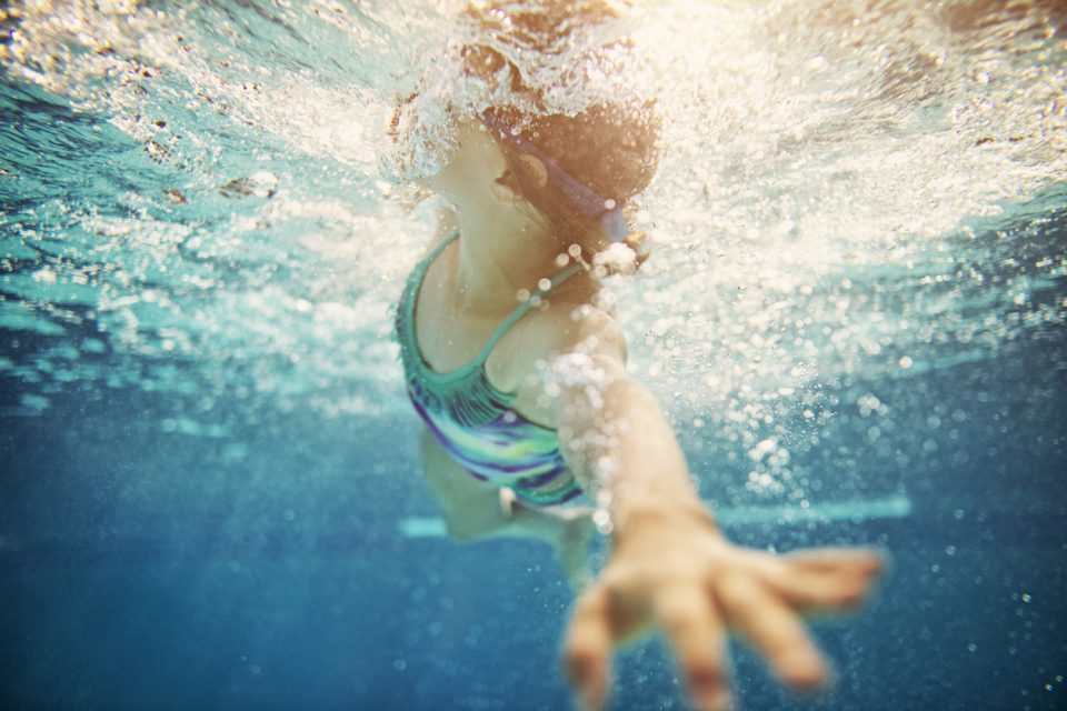 Little girl swimming crawl. Shot from underwater. The girl is reaching towards the camera and taking a breath.